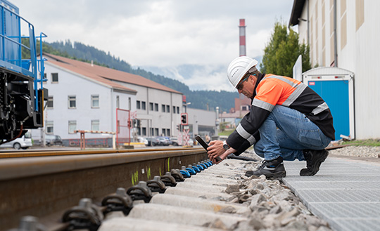 Man sitting next to tracks conducting rail maintenance tasks.