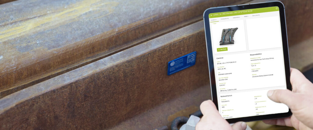 Ein Instandhaltungsmitarbeiter hält ein Tablet zu einem am Bahngleis angebrachten Sensor